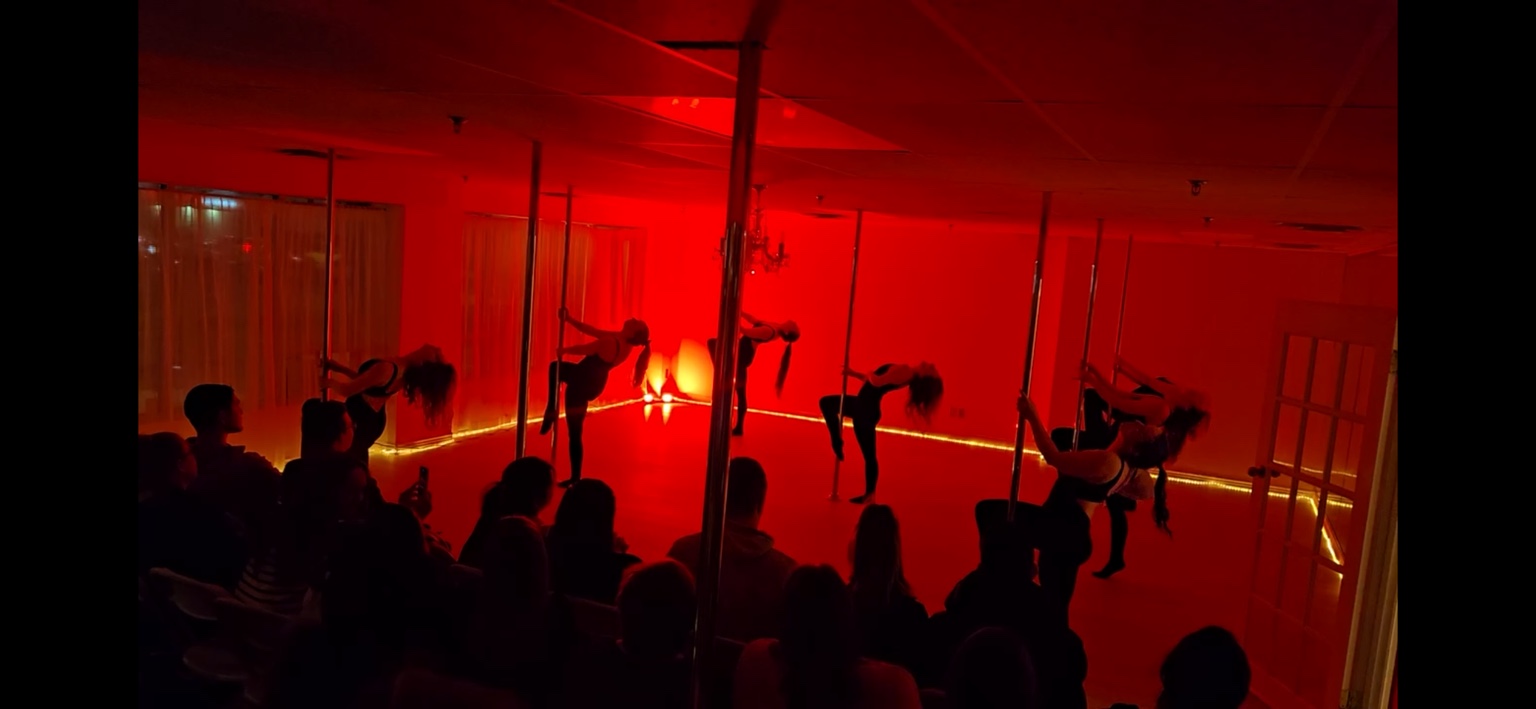 Body Evolution Studios performers dancing together in red light before a showcase audience